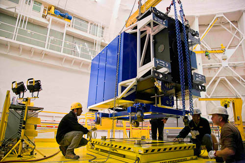 Image of the Canopus adaptive optics system being lowered onto a cart for installation on the Gemini South telescope. The system appears as a large cylindrical object.