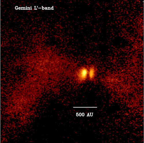 Image of a young star system called L1527.  Shows a bright central disk surrounded by a faint reddish cloud. The bright yellow areas are the surfaces of the disk, separated by a dark lane. The reddish cloud is light scattered from the inner regions of the forming star.
