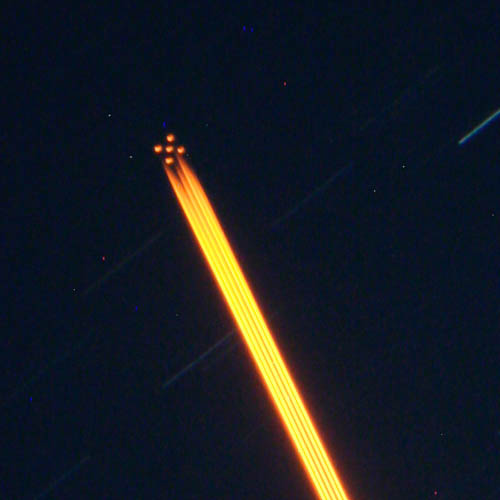 Image of the Gemini South laser guide star system. A constellation-like pattern of artificial stars is seen in the upper left corner. This is created by a laser beam (visible as a yellow-orange streak) shining towards the sky.